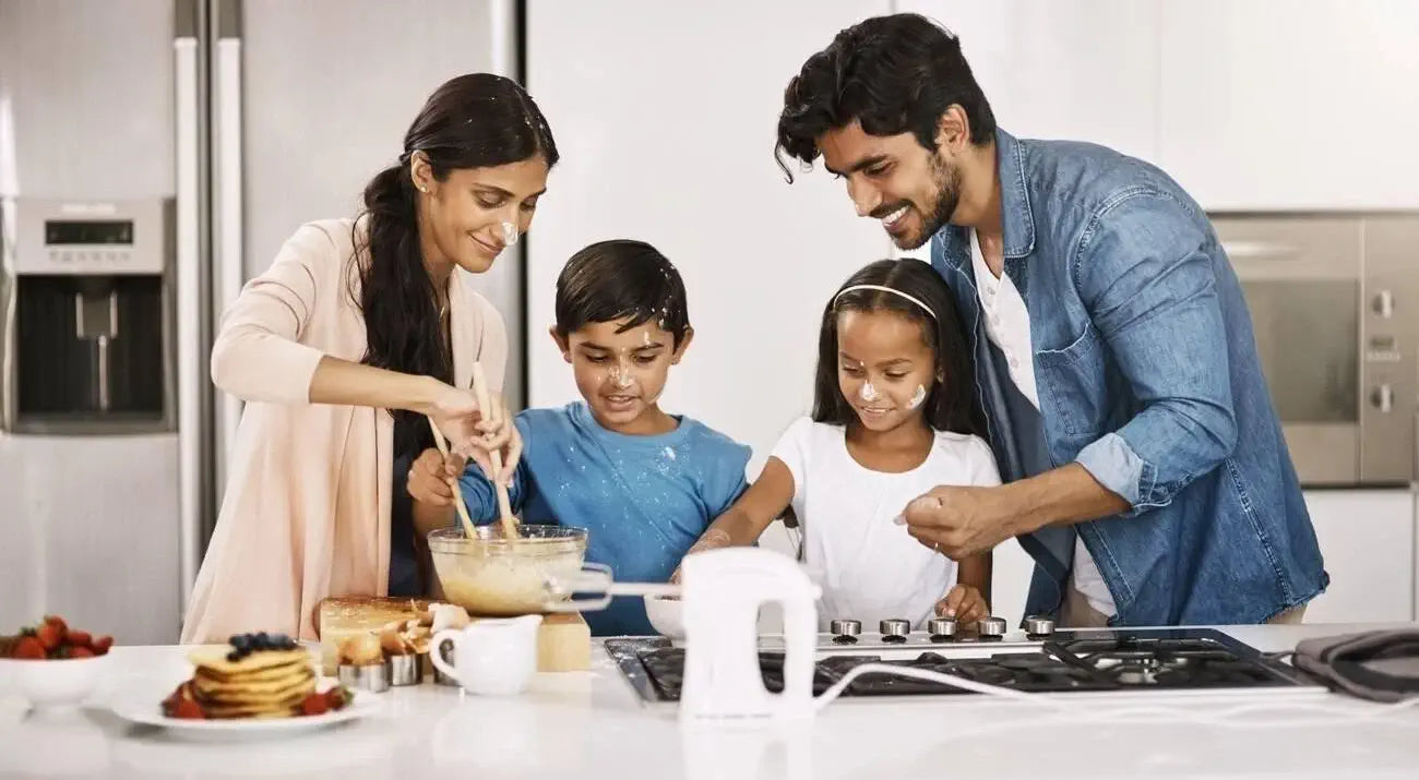 A family of four cooking together in the kitchen, smiling and preparing food with Swasthya Atta.